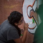 Closeup of a young woman working on the "Color Me Cruces" mural